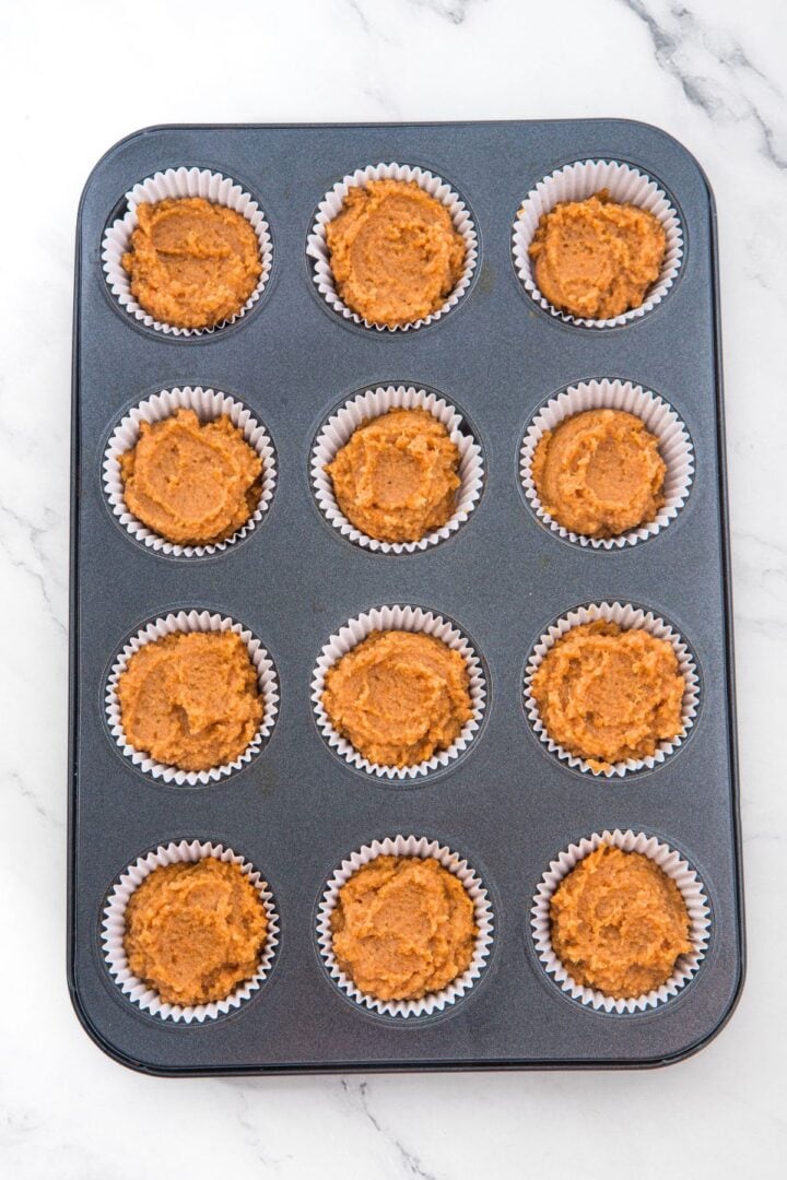 Pumpkin muffin batter in lined muffin pan.