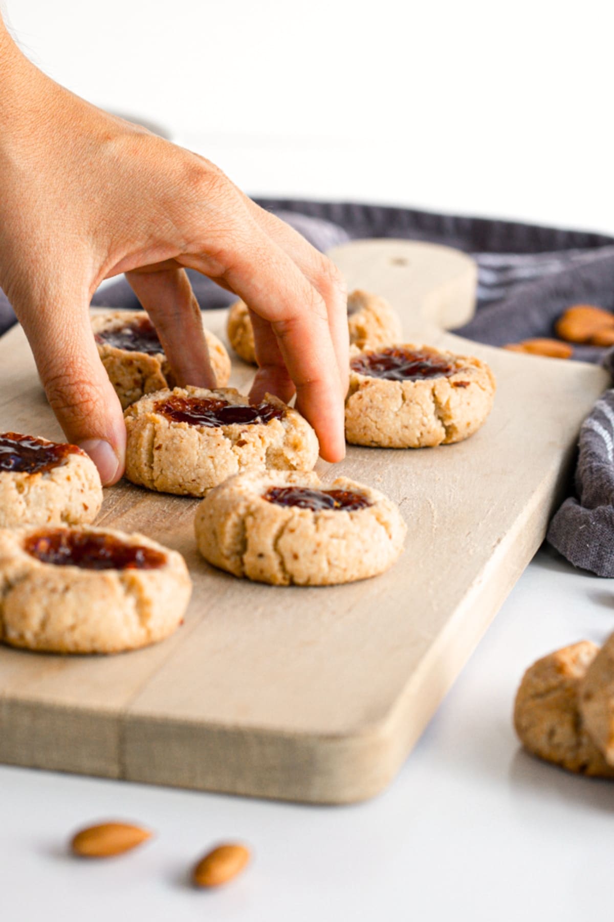 Hand reaching for a thumbprint cookie from wooden board.