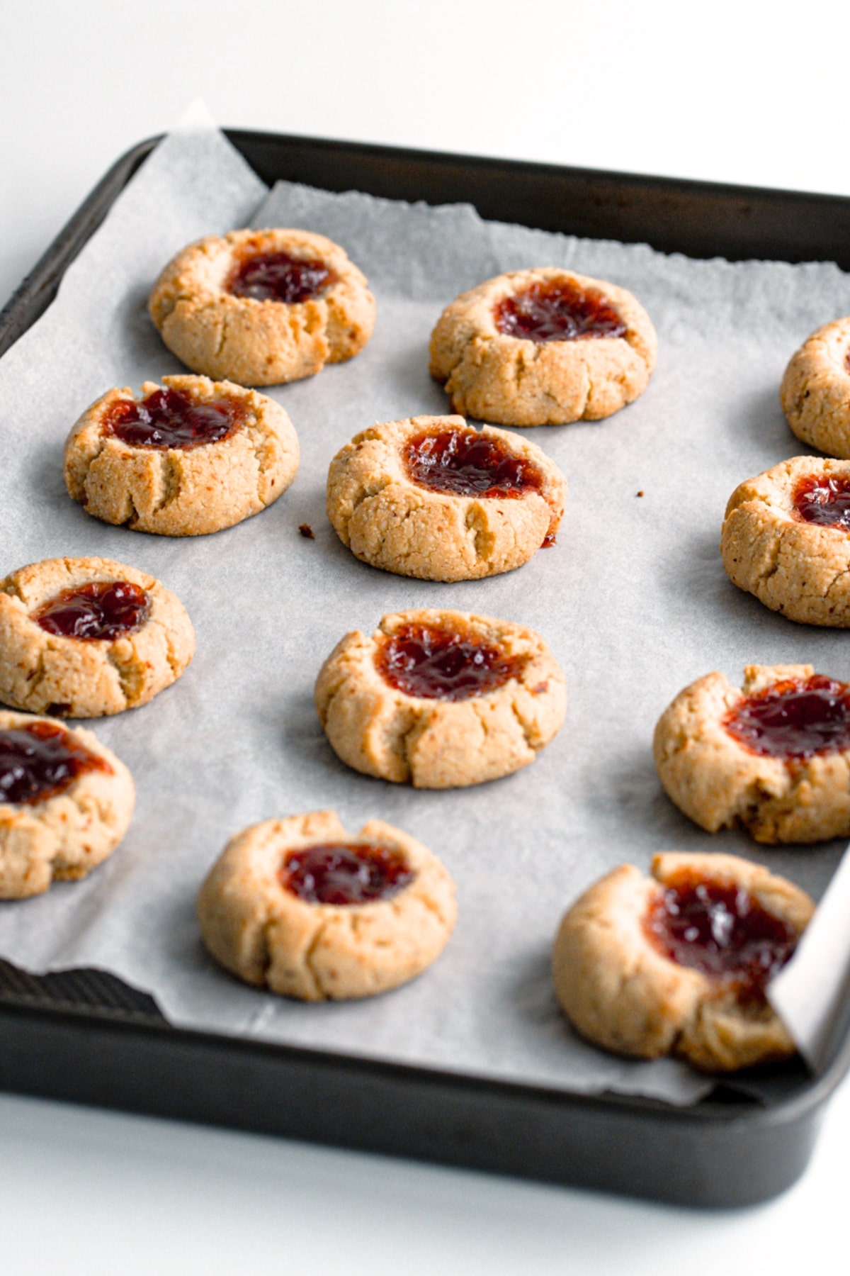 Freshly baked thumbprint cookies on parchment-lined baking tray.