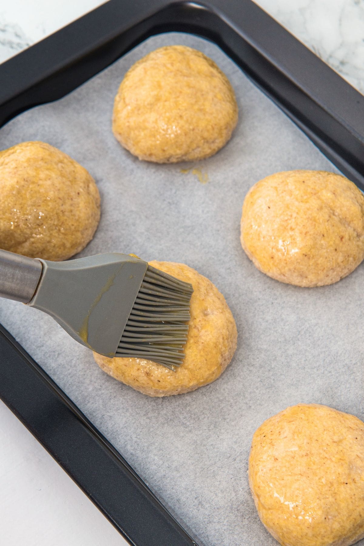 Using silicon brush to brush balls of bread dough with egg yolk