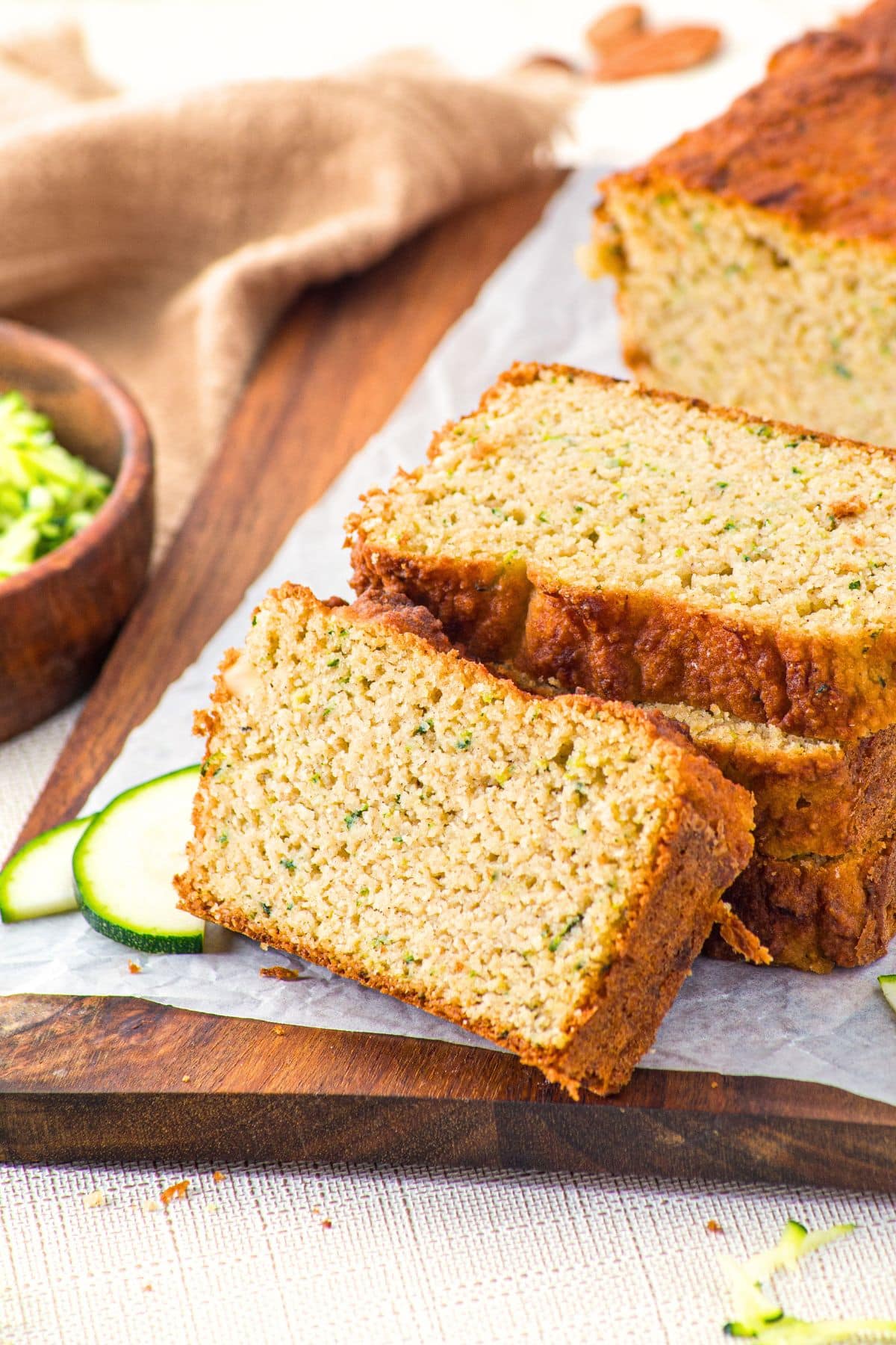 A sliced loaf of almond flour zucchini bread on parchment-lined board.