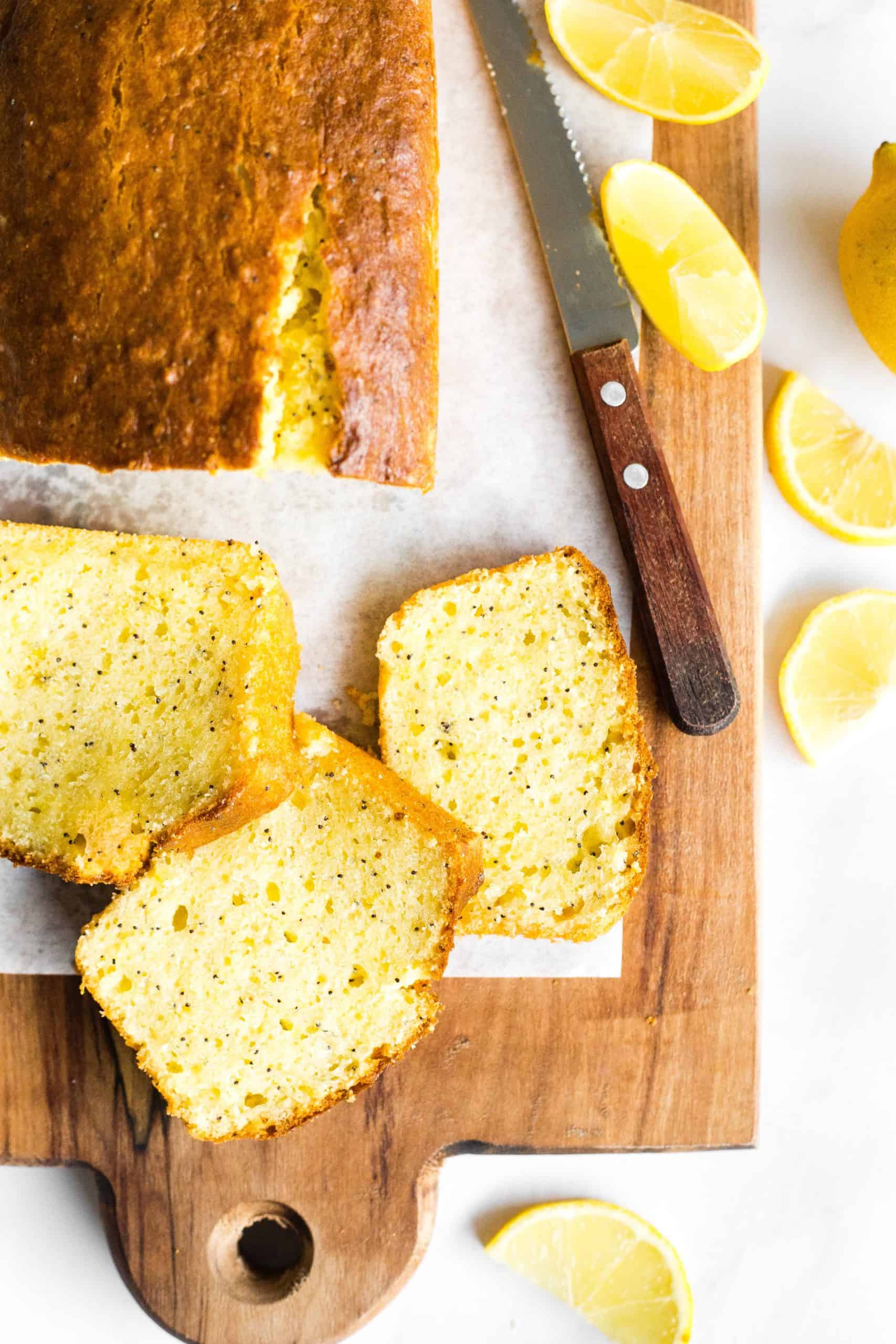 A sliced loaf of gluten-free lemon poppy seed cake on a wooden board.