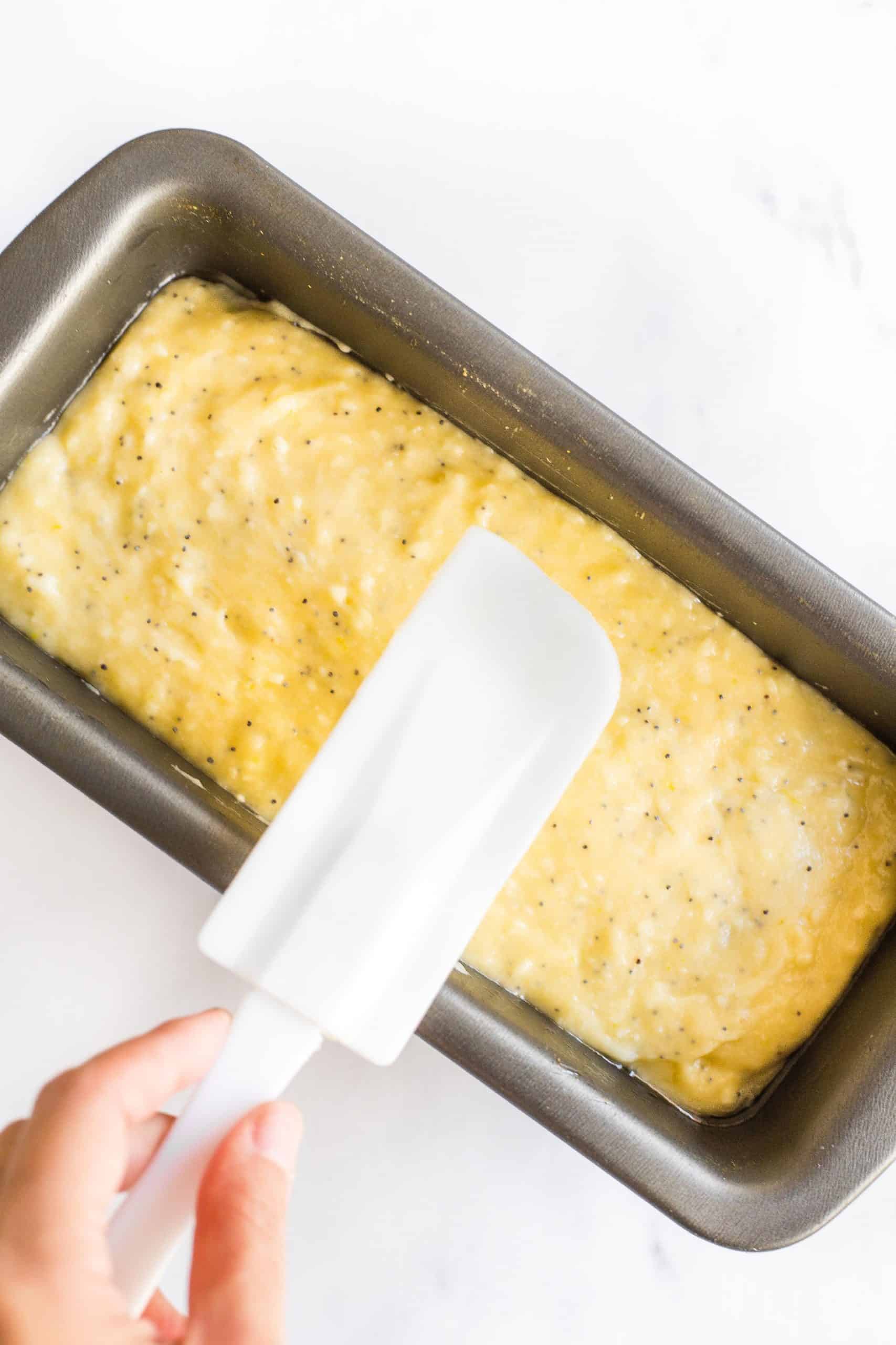 Using a spatula to smooth out the batter in a loaf pan.