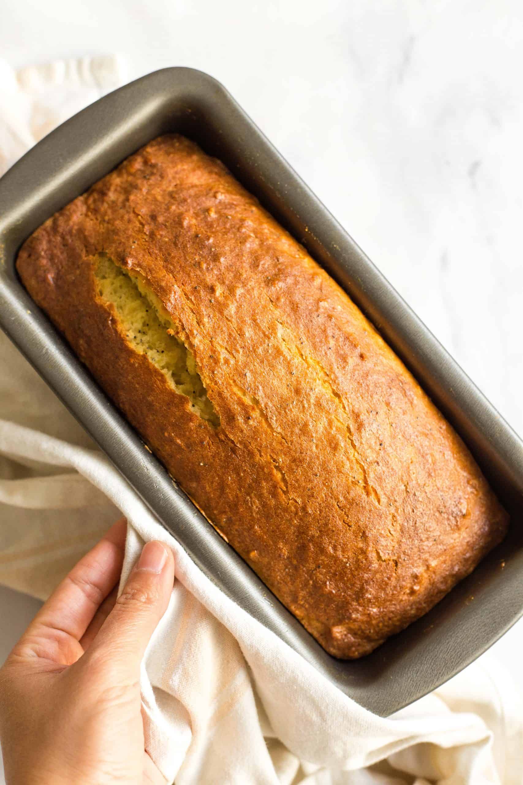 Holding a metal loaf pan with a freshly baked loaf of gluten-free poppy seed bread.
