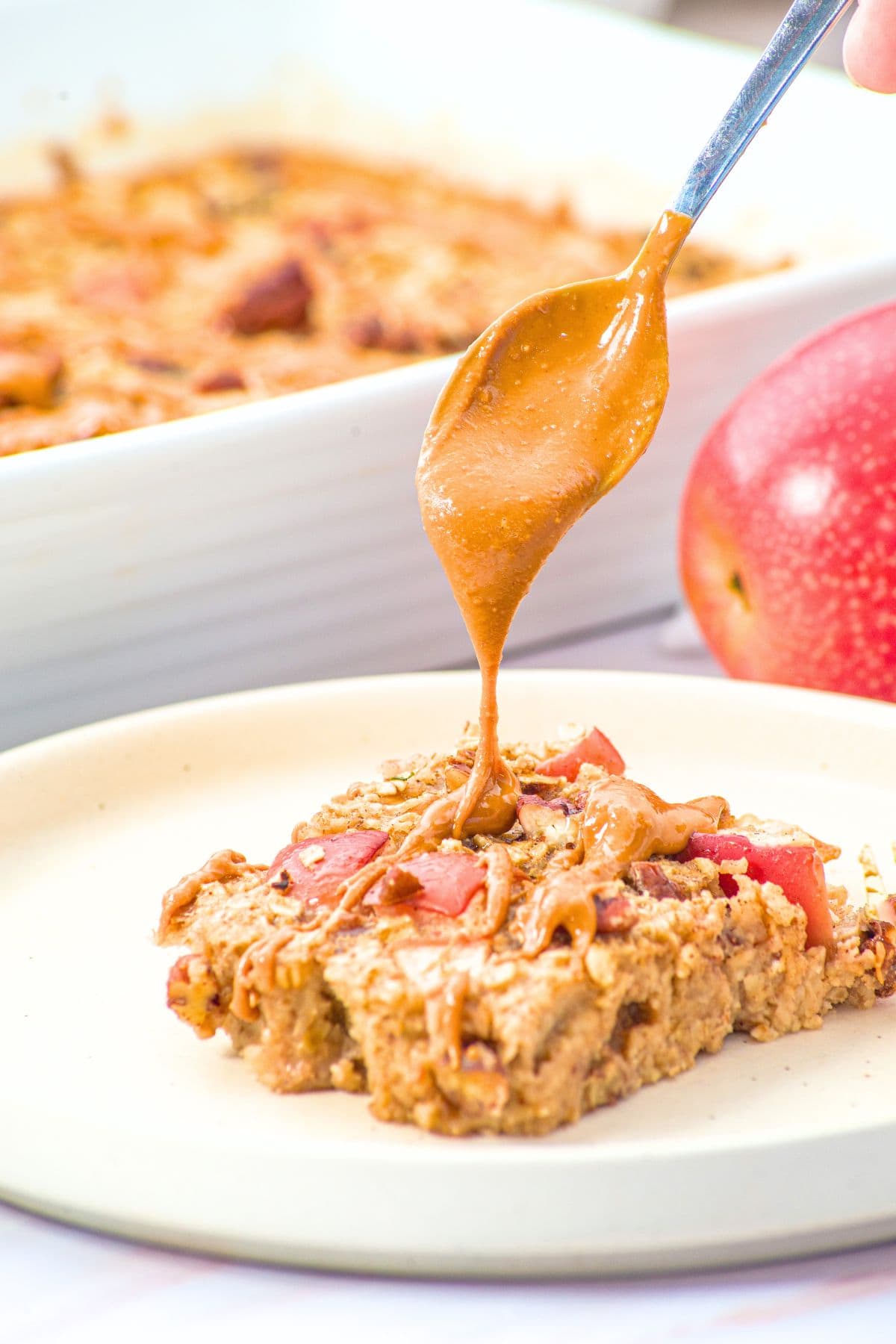 Drizzling almond butter onto a slice of baked oatmeal with apples and cinnamon