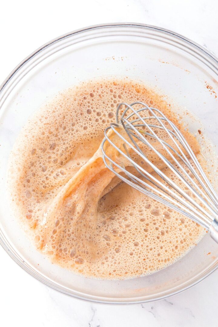 Whisking brown liquid mixture in glass bowl