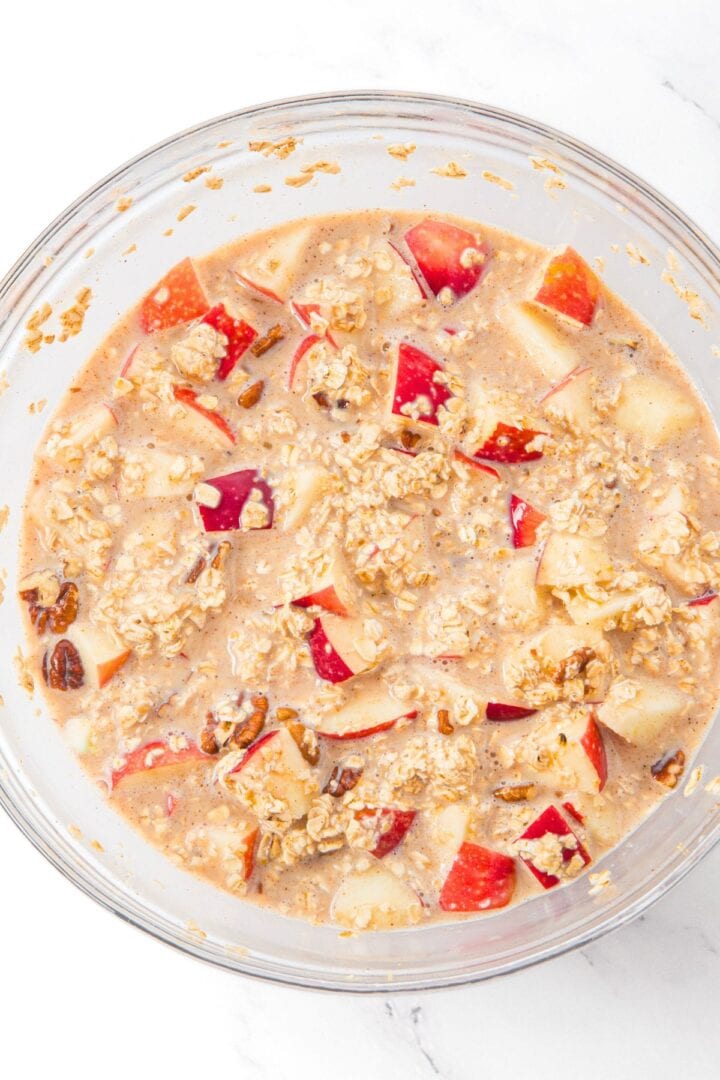 A bowl with mixture of oats, diced apples, chopped pecans and brown liquid mixture