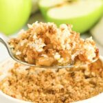 Holding up a spoonful of apple crumble from ramekin