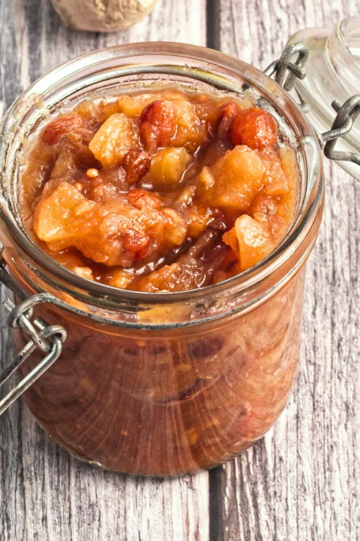 A jar of apple chutney on wooden board.