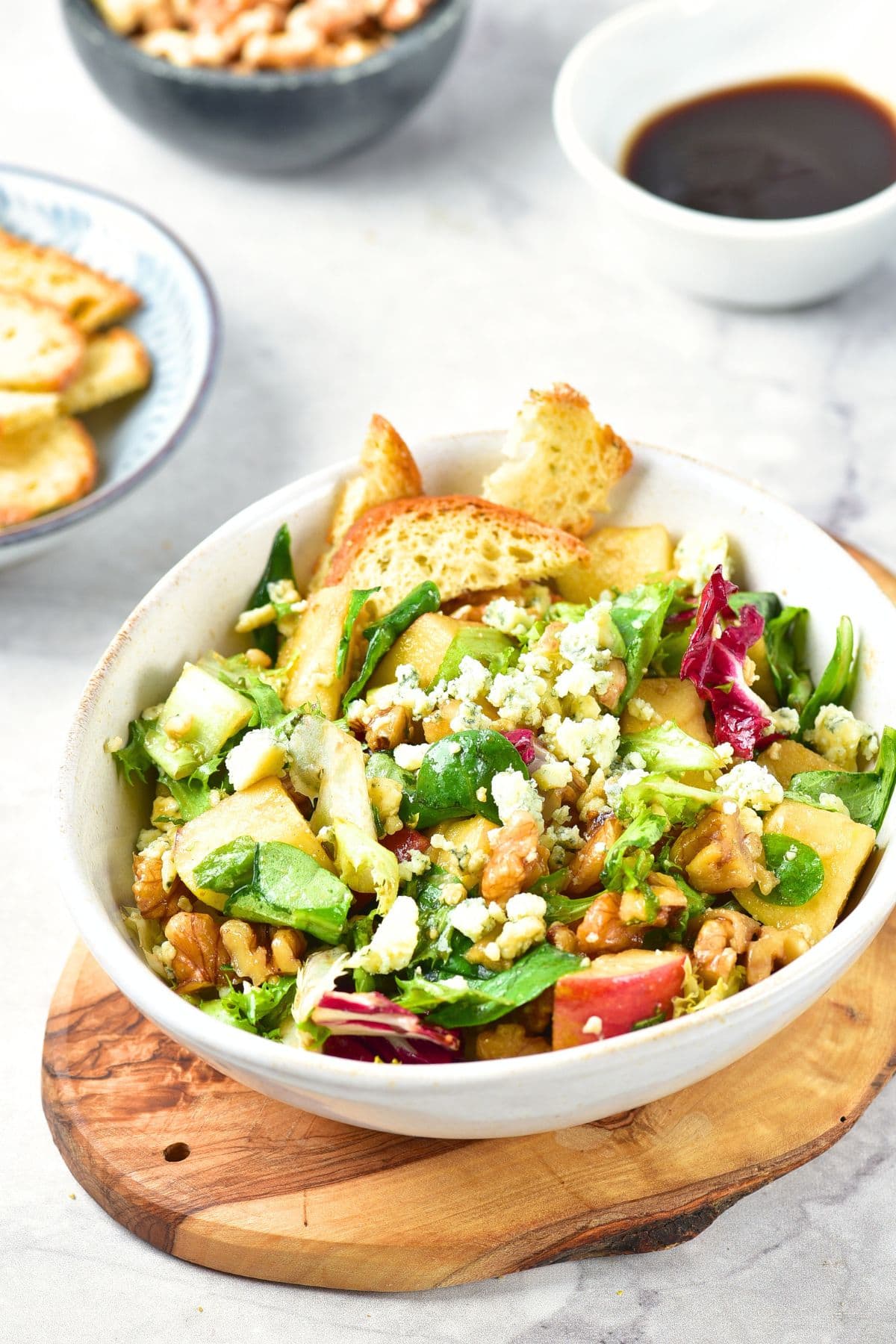 A bowl of apple walnut blue cheese salad on wooden board