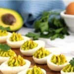 View of guacamole deviled eggs on wooden board.