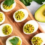 Avocado deviled eggs on wooden board.