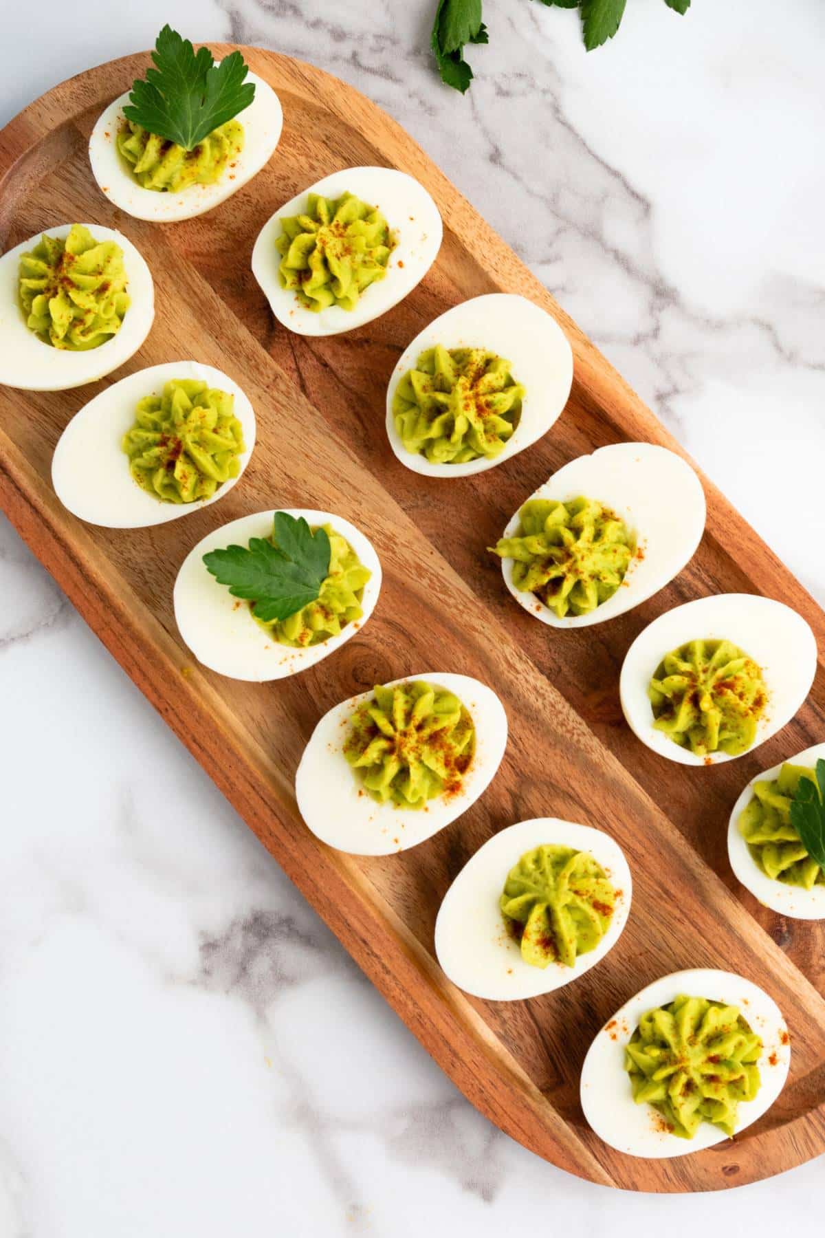 Top down view of deviled eggs with avocado on wooden board.