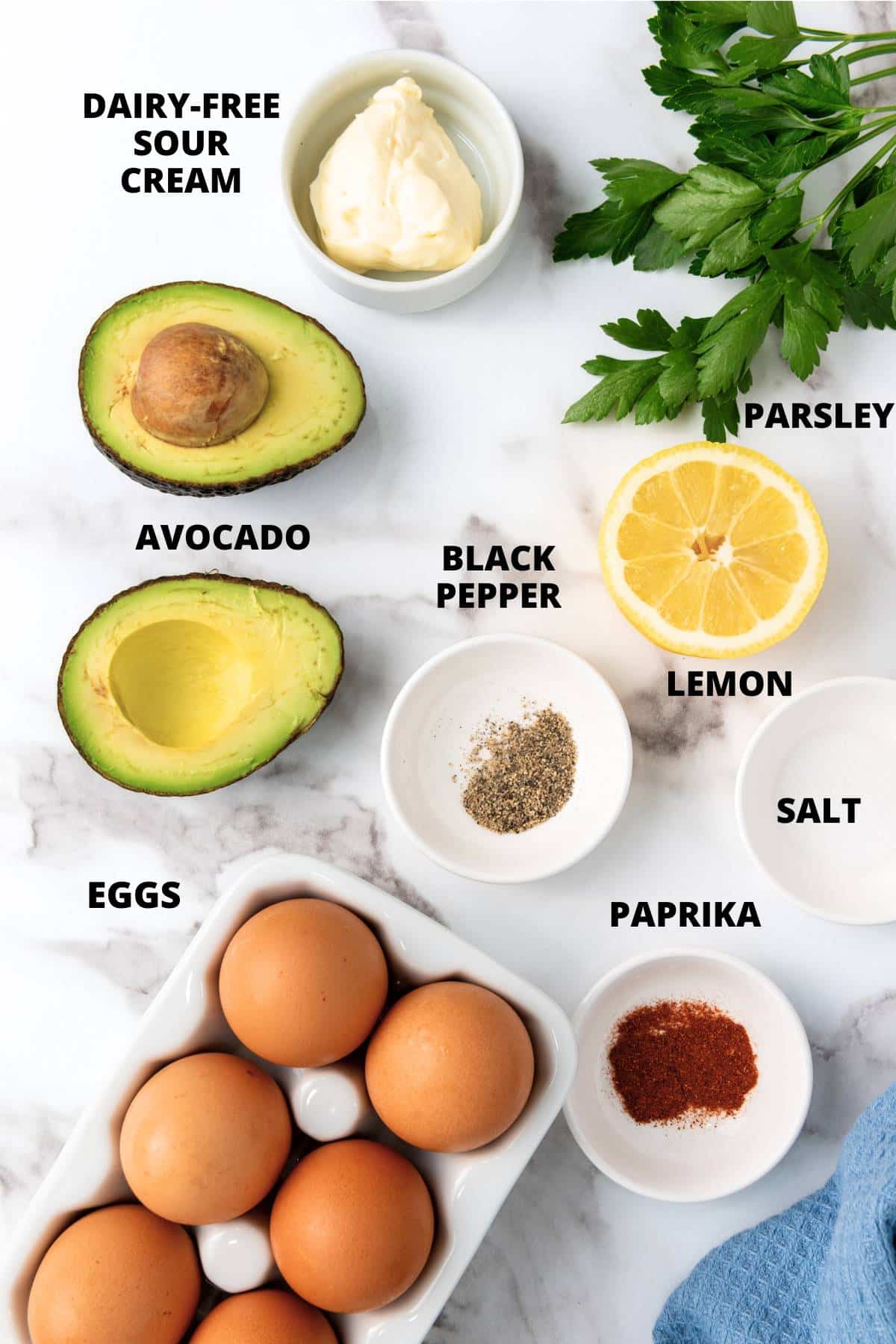 Top down view of ingredients required for avocado deviled eggs recipe laid out on marble board.