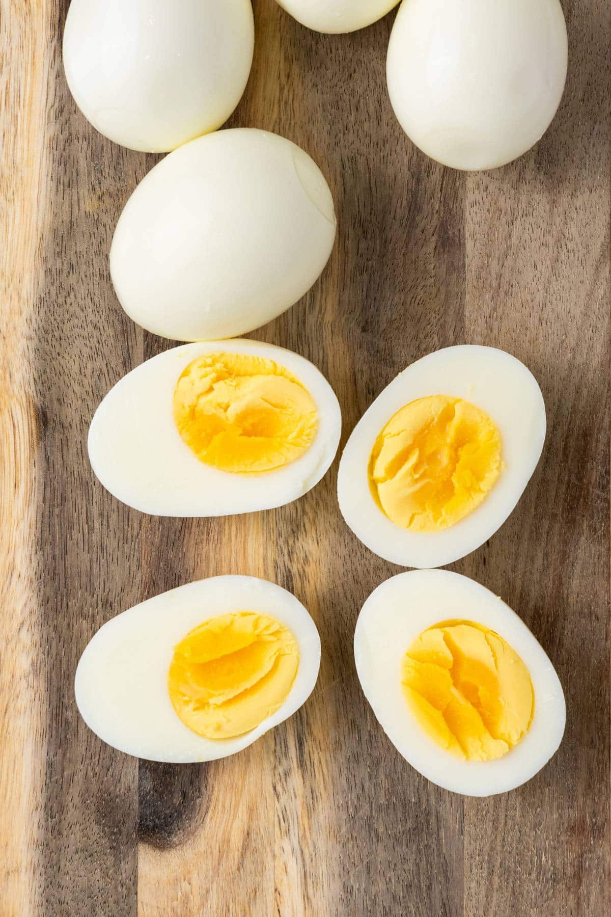 Hard boiled eggs sliced lengthwise on wooden board.
