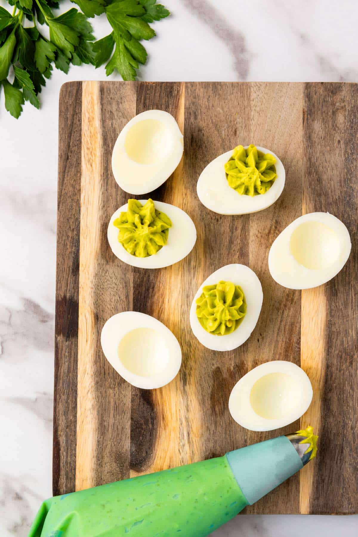 Piping avocado egg yolkd filling into egg white cavities.