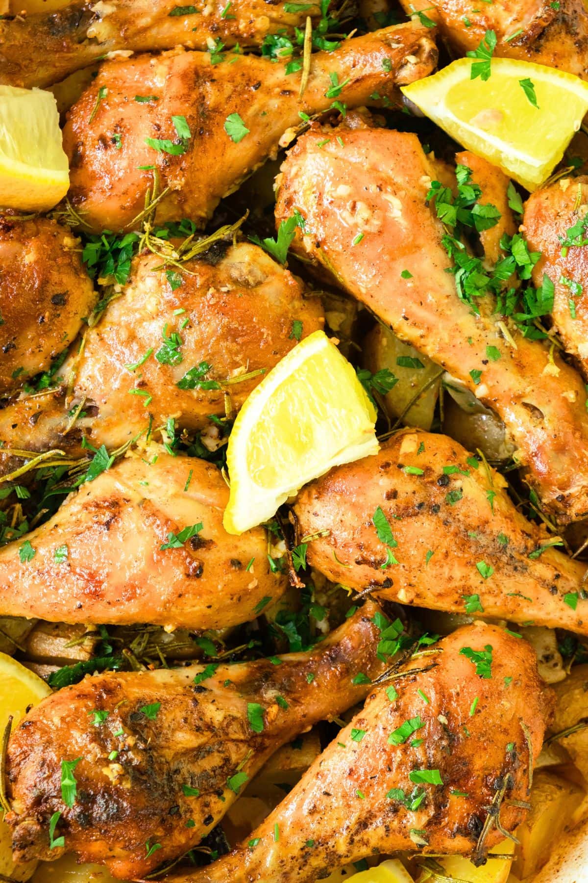 Up close view of baked chicken legs topped with chopped parsley and lemon wedges.
