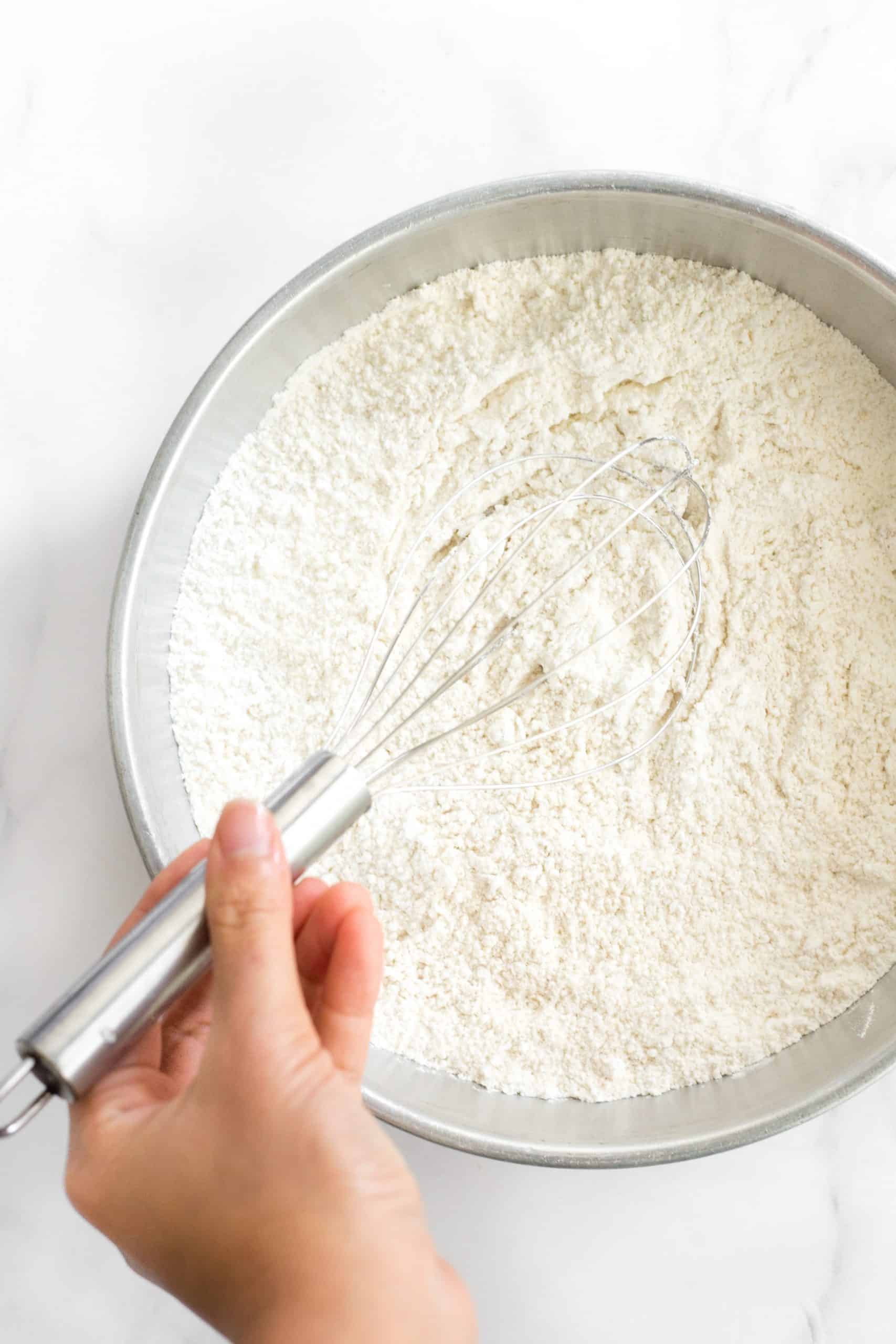 Hand whisking dry ingredients in a metal bowl.