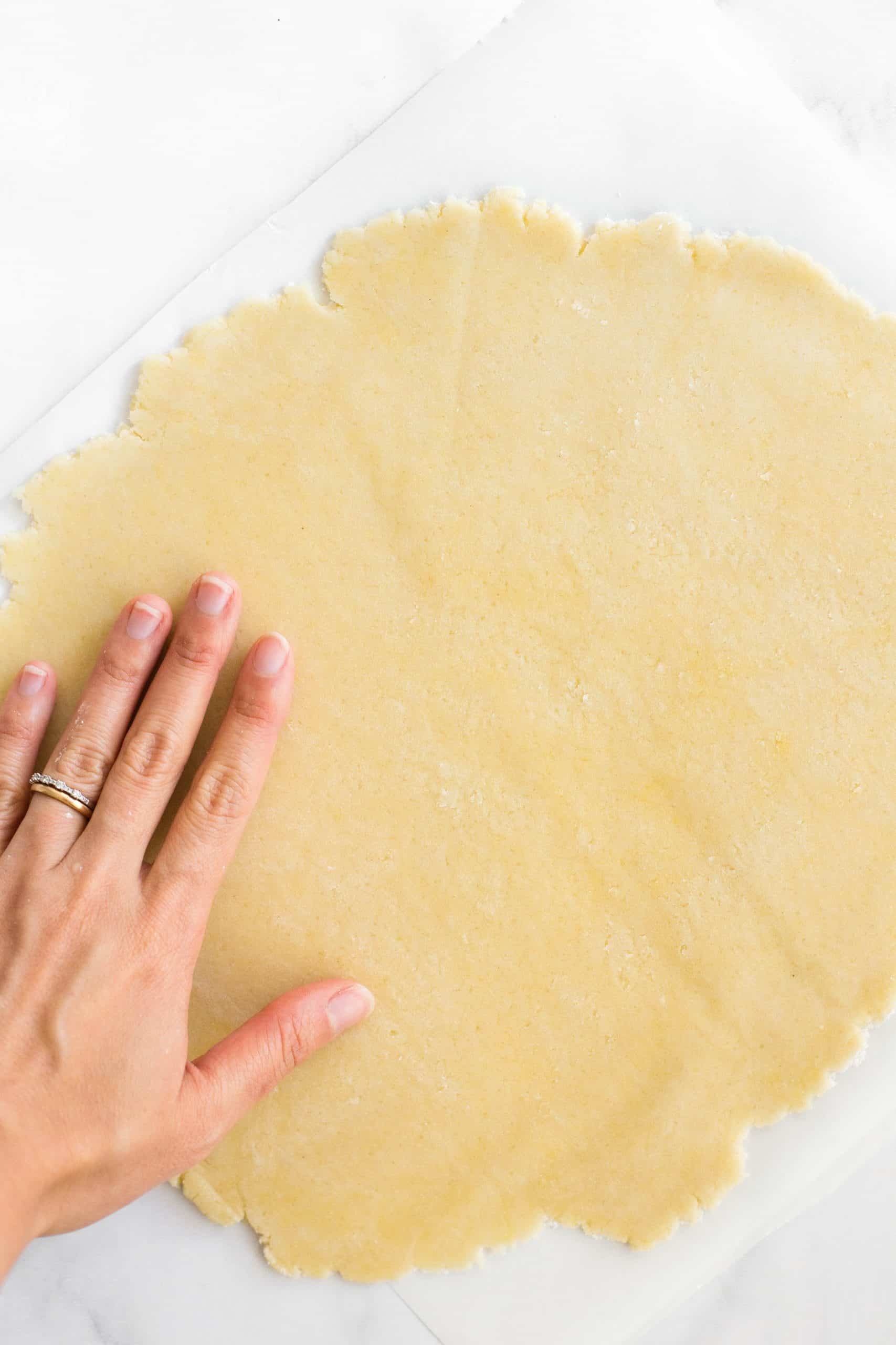 Hand pressing out pie crust dough on parchment paper.