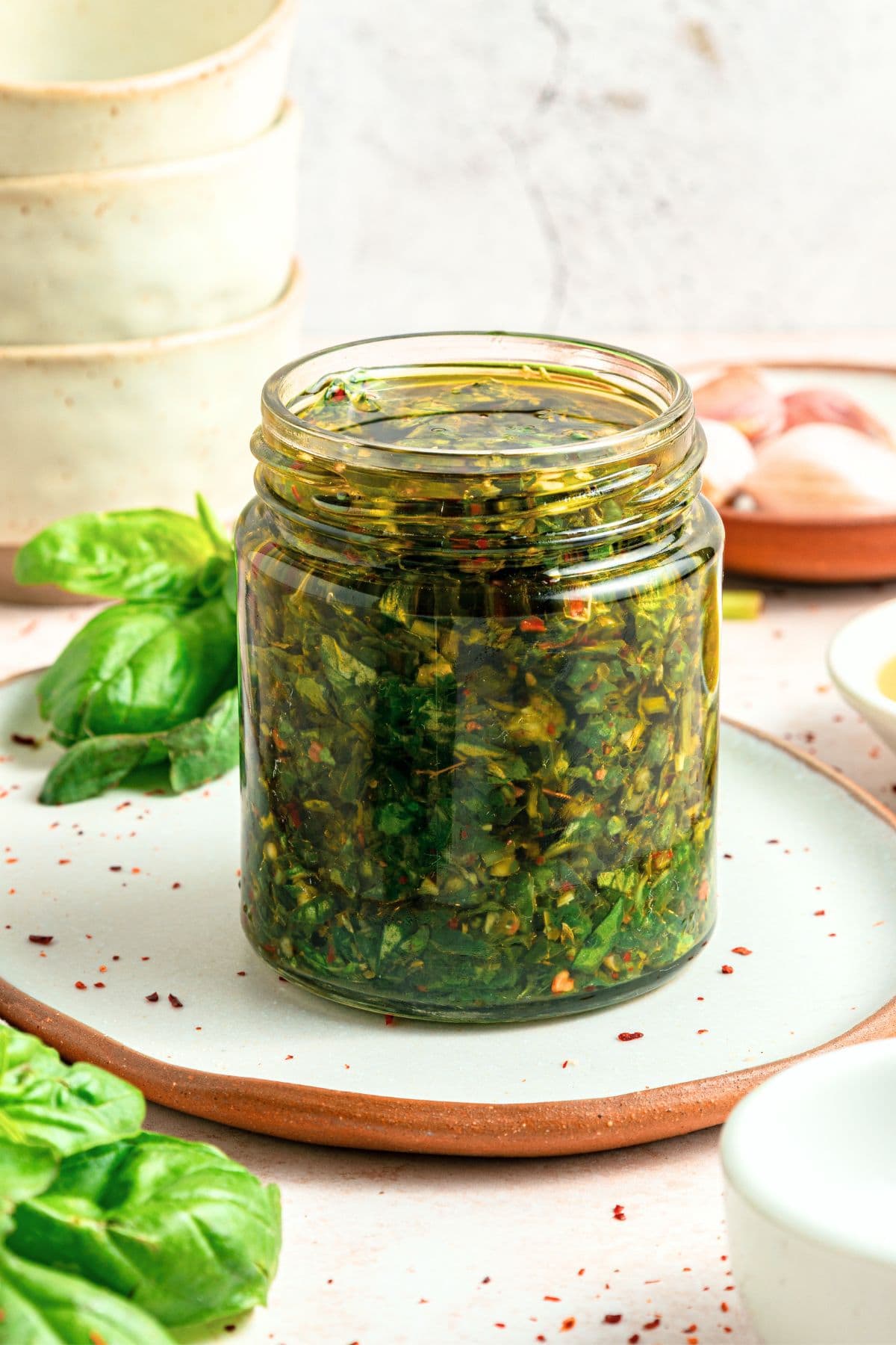 A jar of chimichurri with basil on a plate