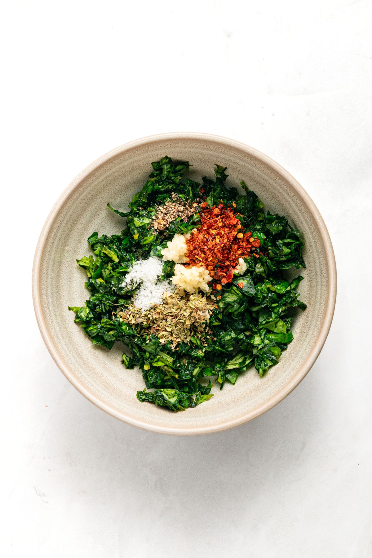 Chopped basil, dried oregano, red pepper flakes, salt, and chopped garlic in a bowl.