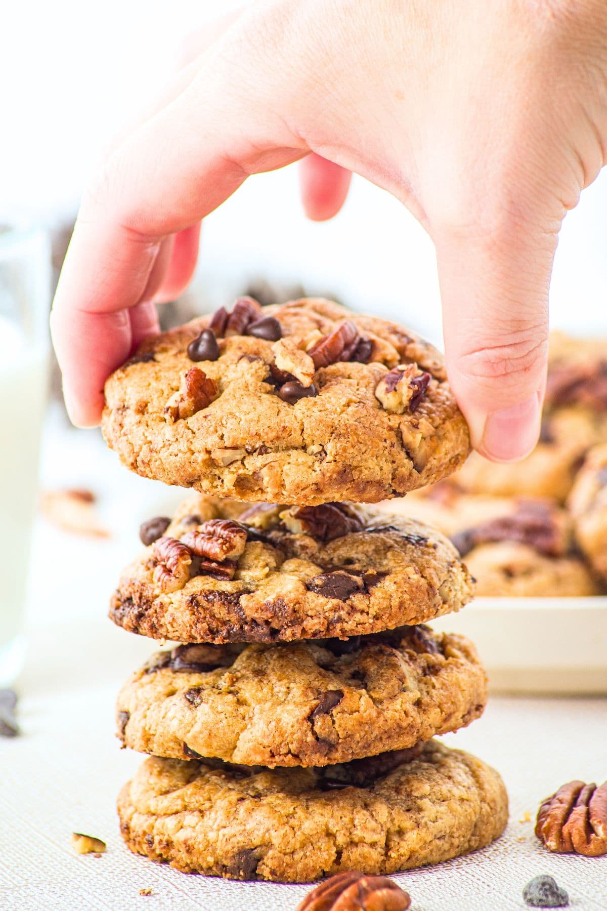 Hand reaching for a stack of brown butter chocolate chip pecan cookies