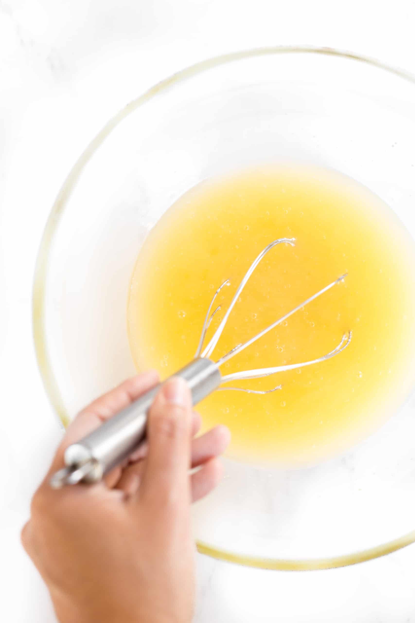 Whisking yellow mixture in a glass bowl.
