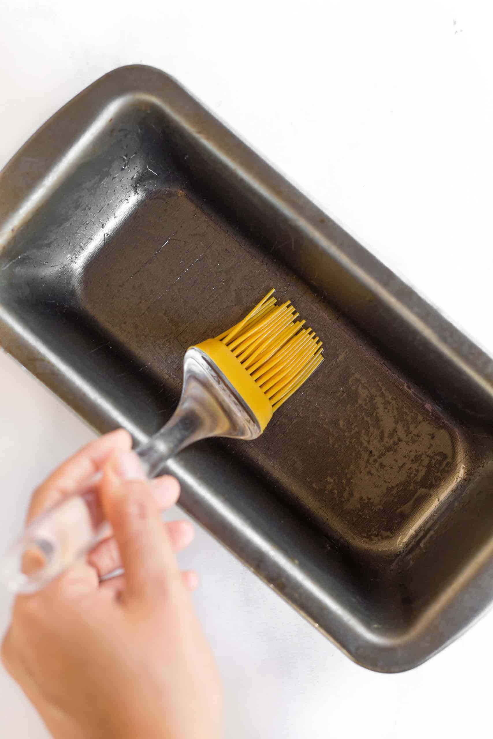 Using a silicon brush to grease metal loaf pan.