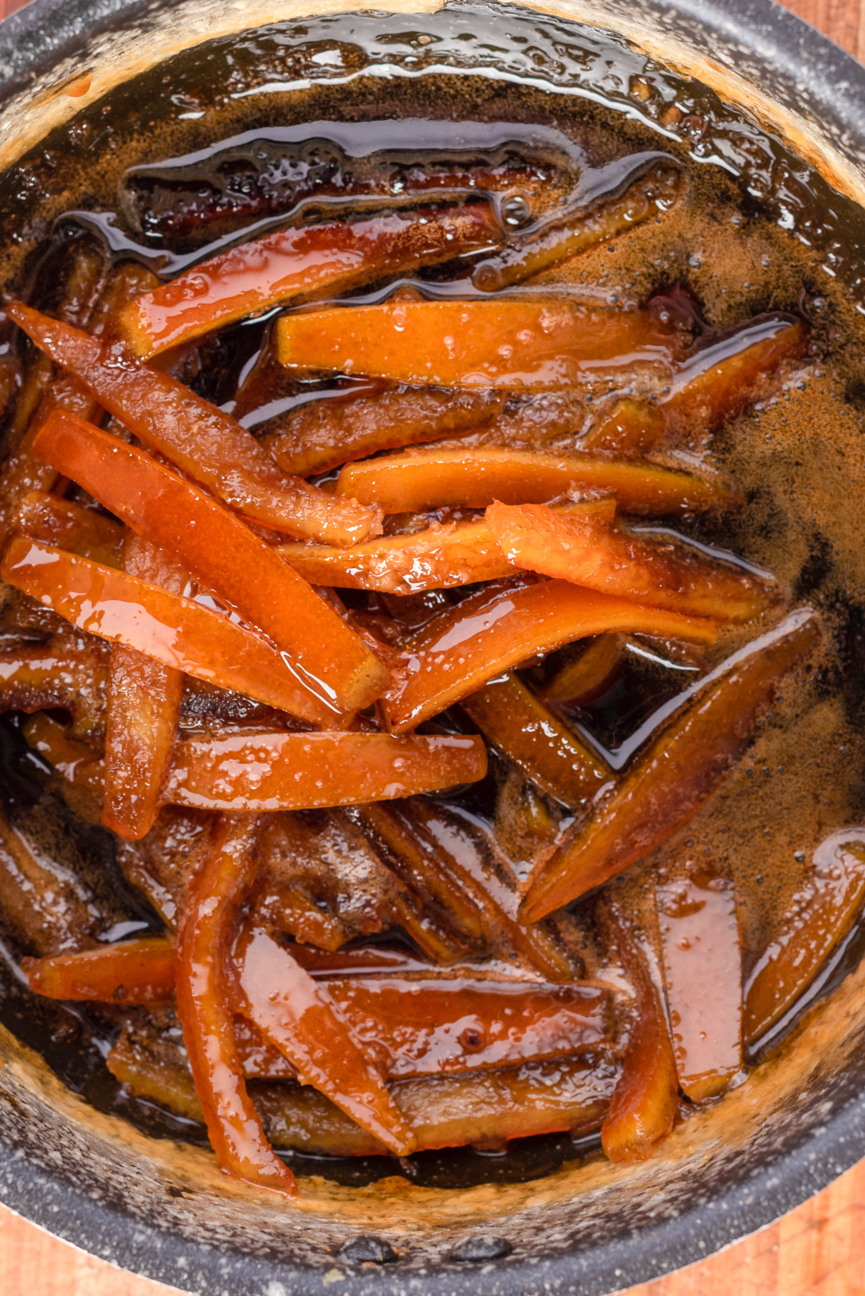 Orange peels boiling in sugar syrup in a pot.