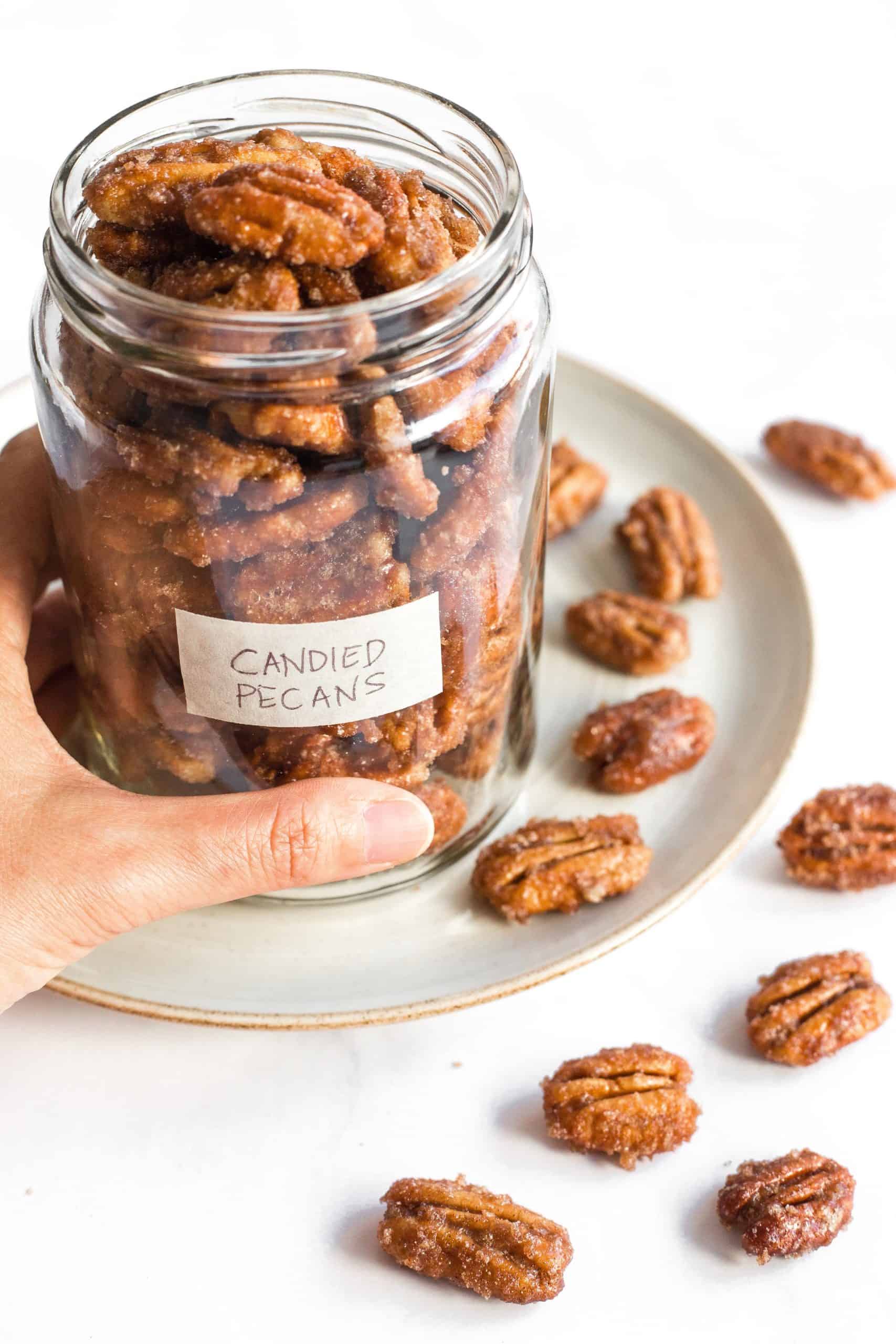 Hand holding a jar full of stovetop candied pecans.