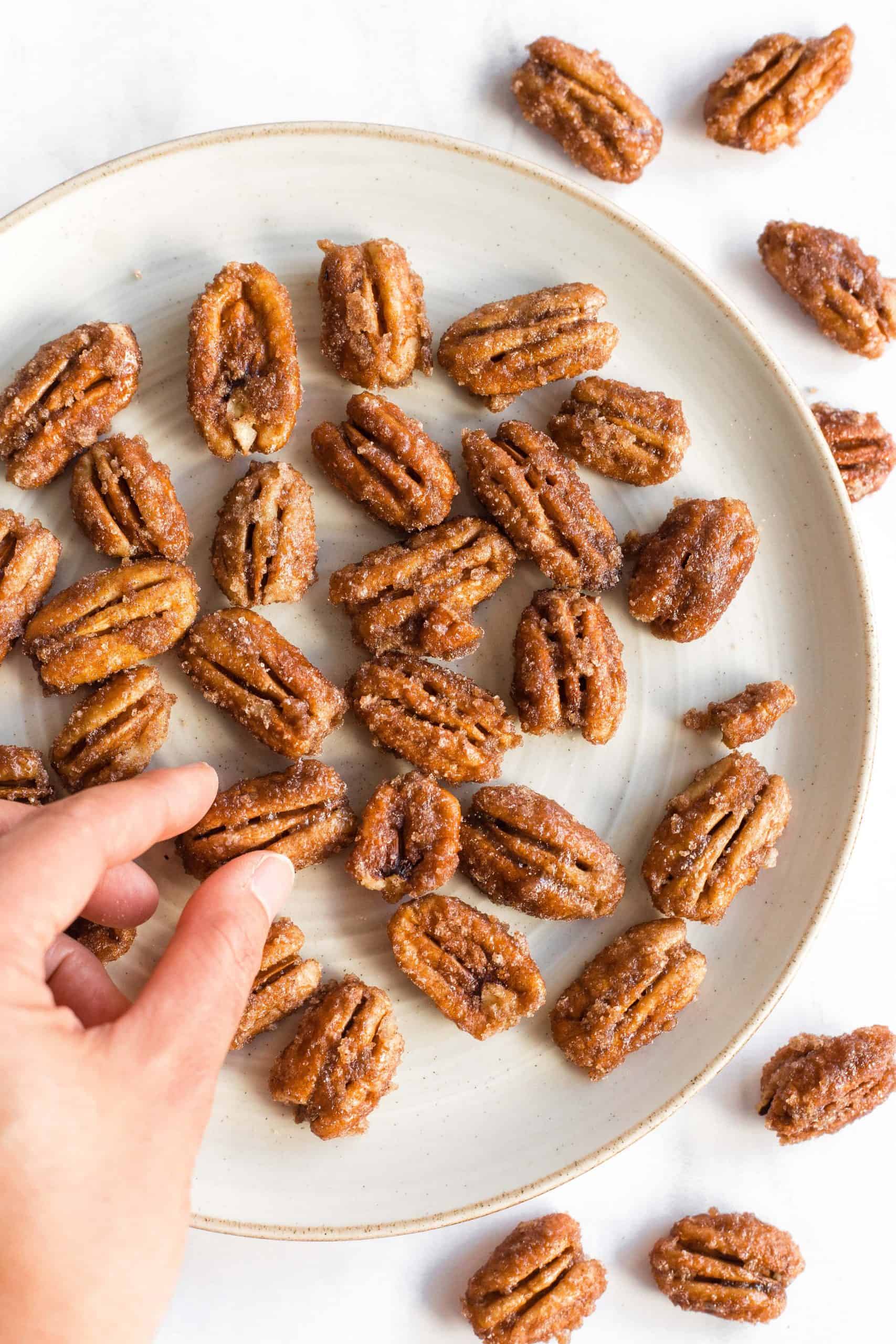 Picking up a pecan from a plate full of candied pecans.