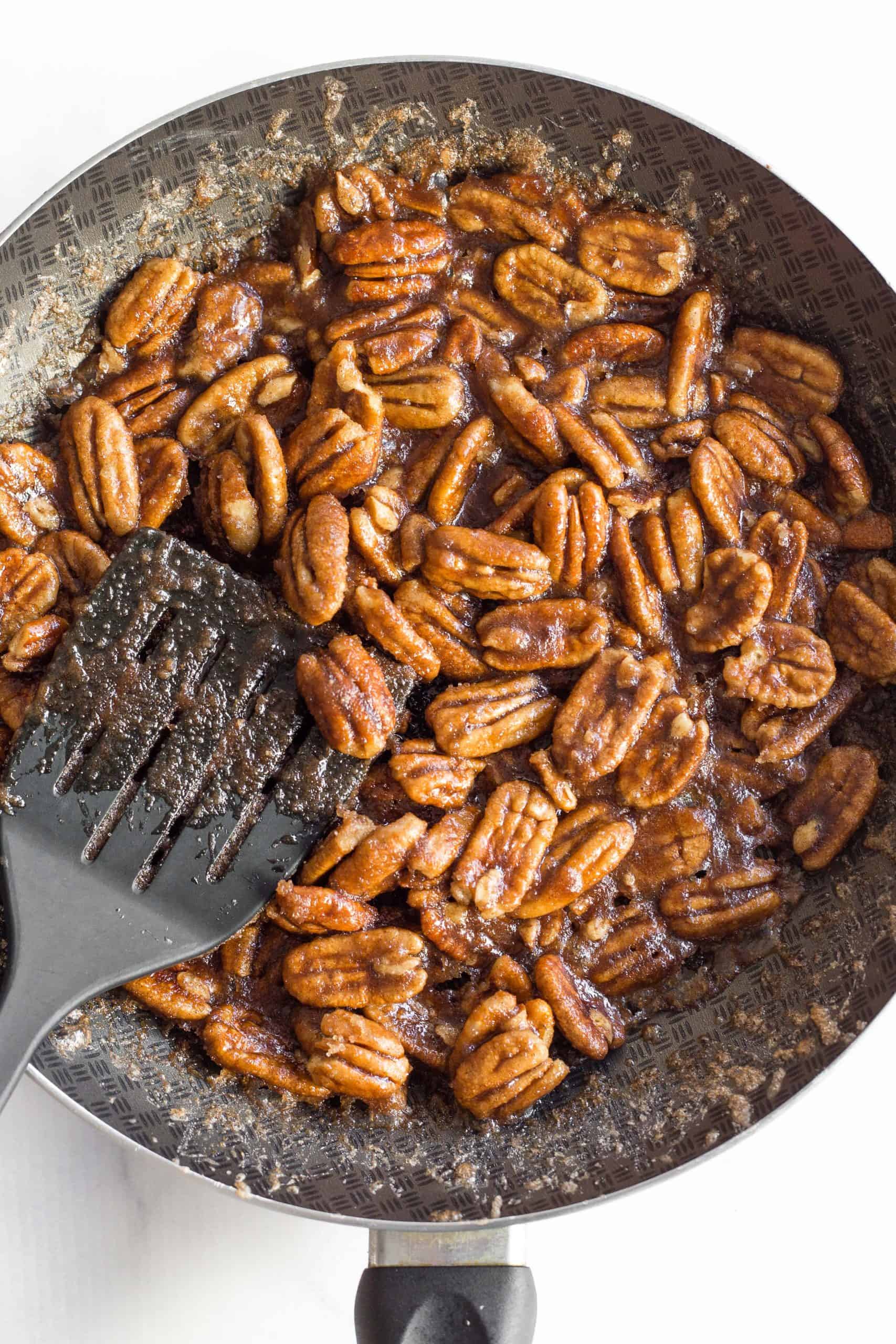 A skillet full of pecans coated with a sugar mixture.