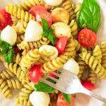 Fork reaching into plate of caprese pesto pasta salad.