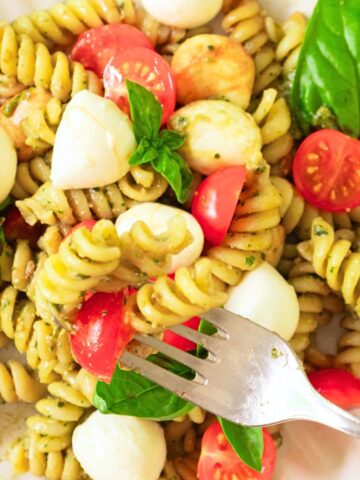 Fork reaching into plate of caprese pesto pasta salad.
