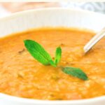 Up close view of a bowl of carrot lentil soup topped with mint.
