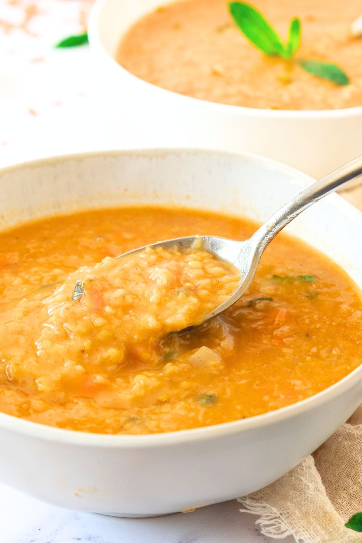 Holding a spoonful of carrot red lentil soup.