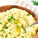 A spoon in a bowl of mashed potatoes and cauliflower