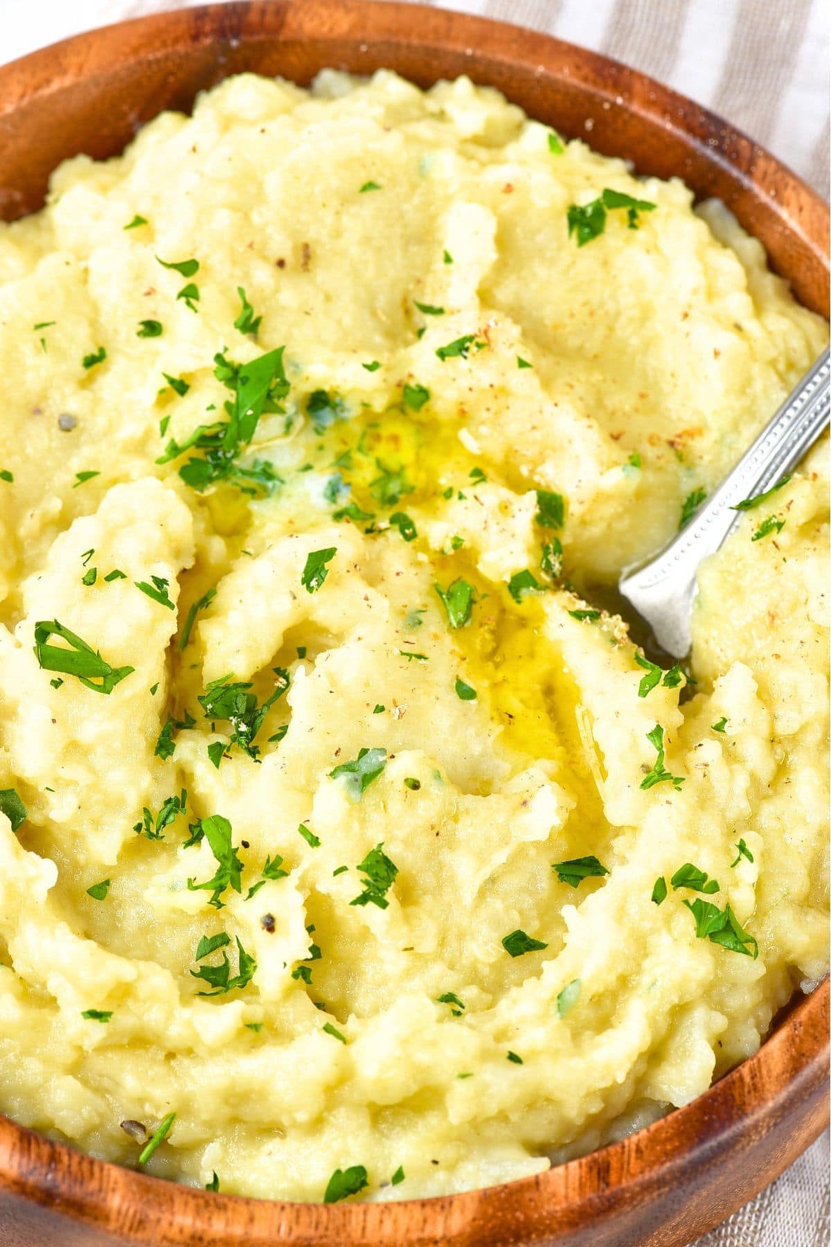 A spoon in a bowl of cauliflower potato mash topped with parsley