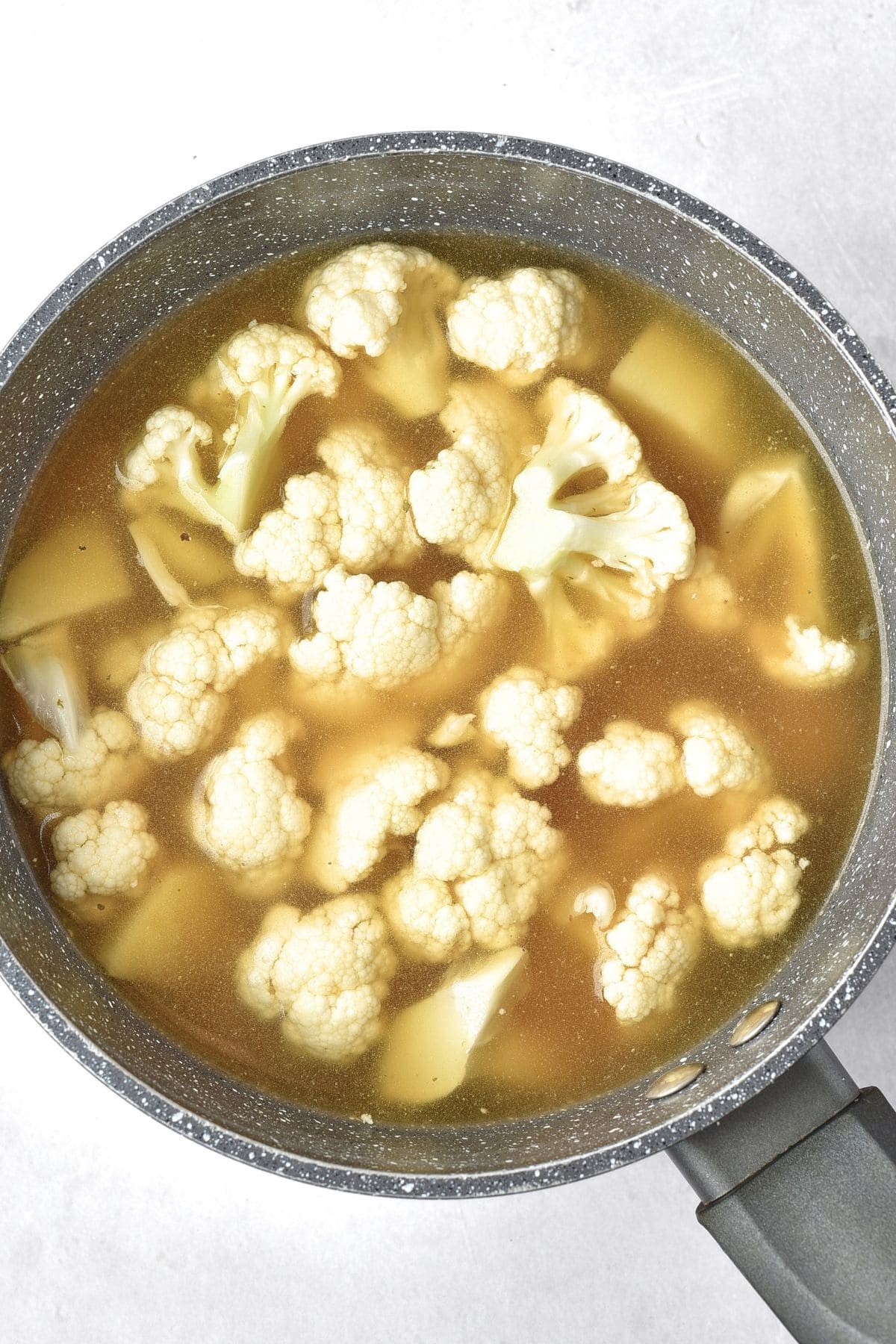 Boiling cauliflower florets and potato cubes in vegetable stock
