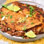 A plate of birria tacos with lime wedges.