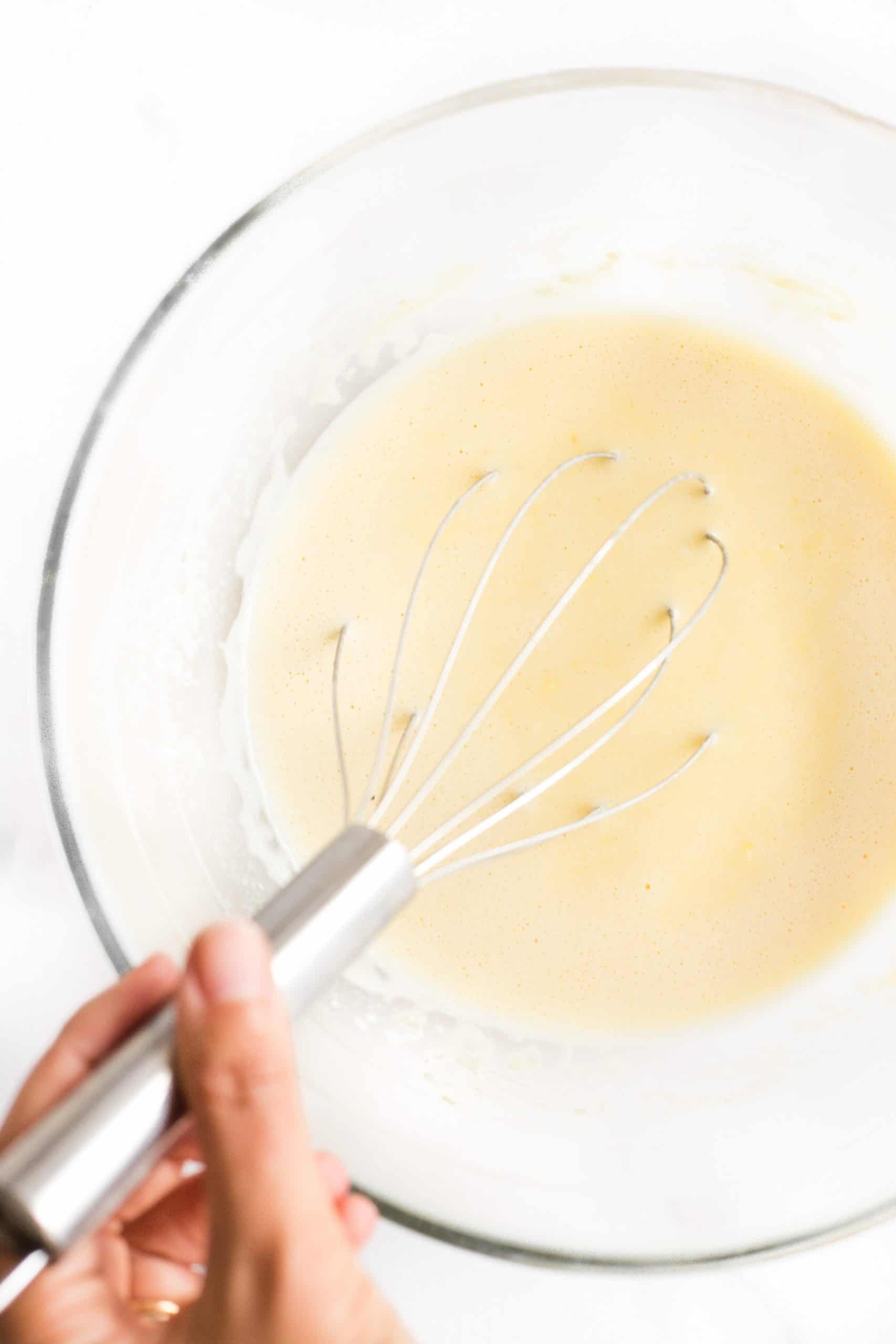 Hand whisking batter in a glass bowl.