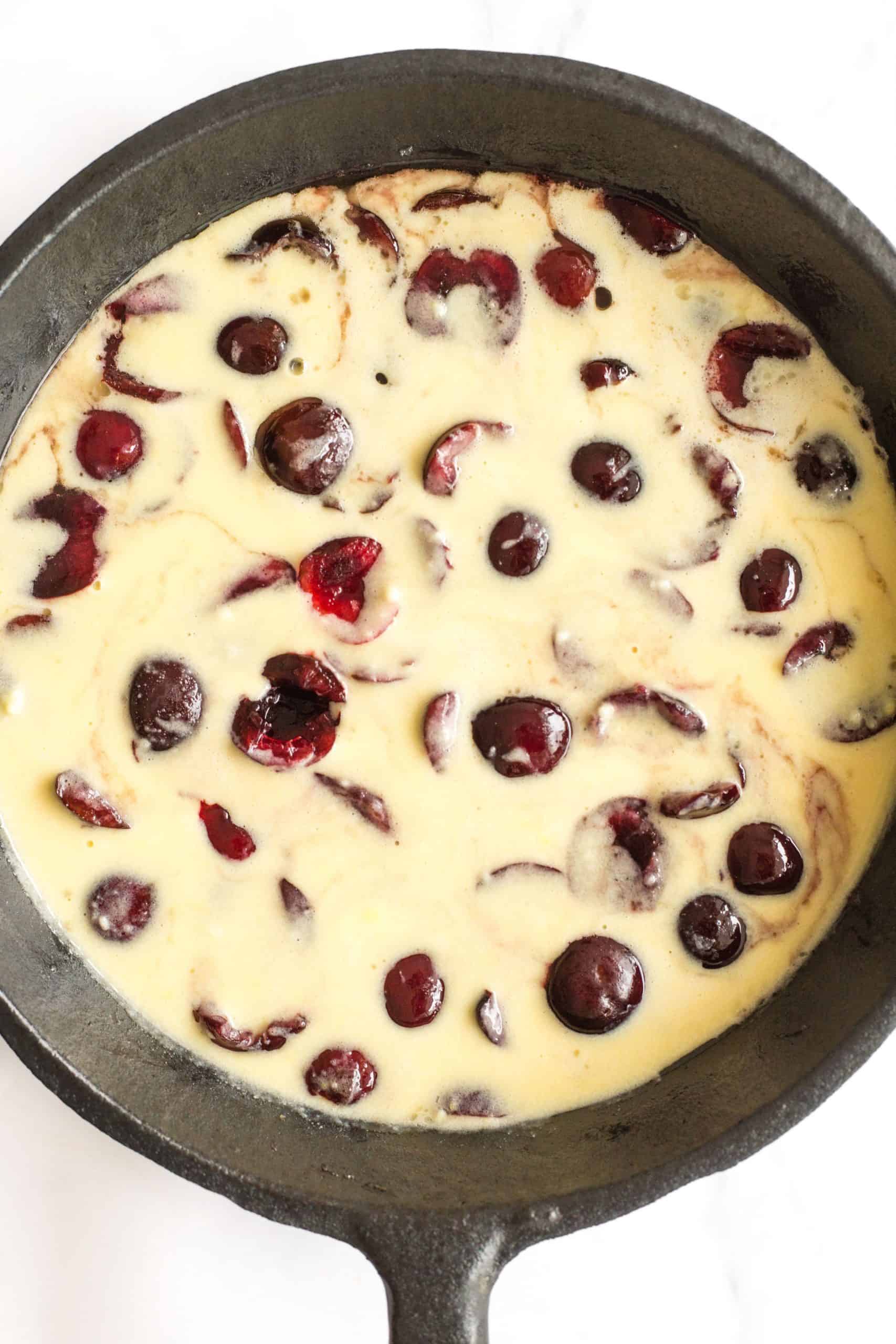 Cherries in raw batter in a cast iron skillet.
