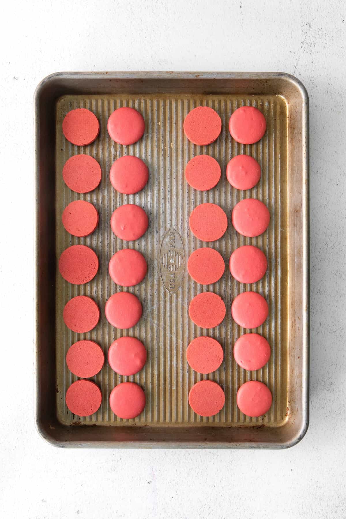 Freshly baked red macaron shells cooling on baking sheet.