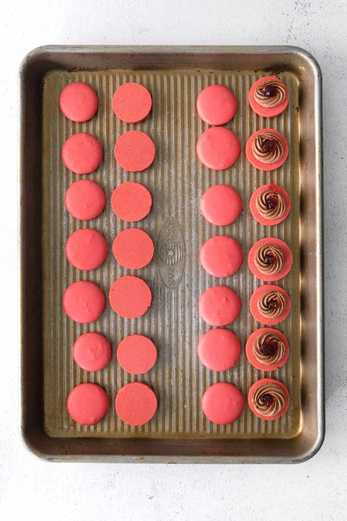 Red macaron shells topped with chocolate buttercream and cherry jam.