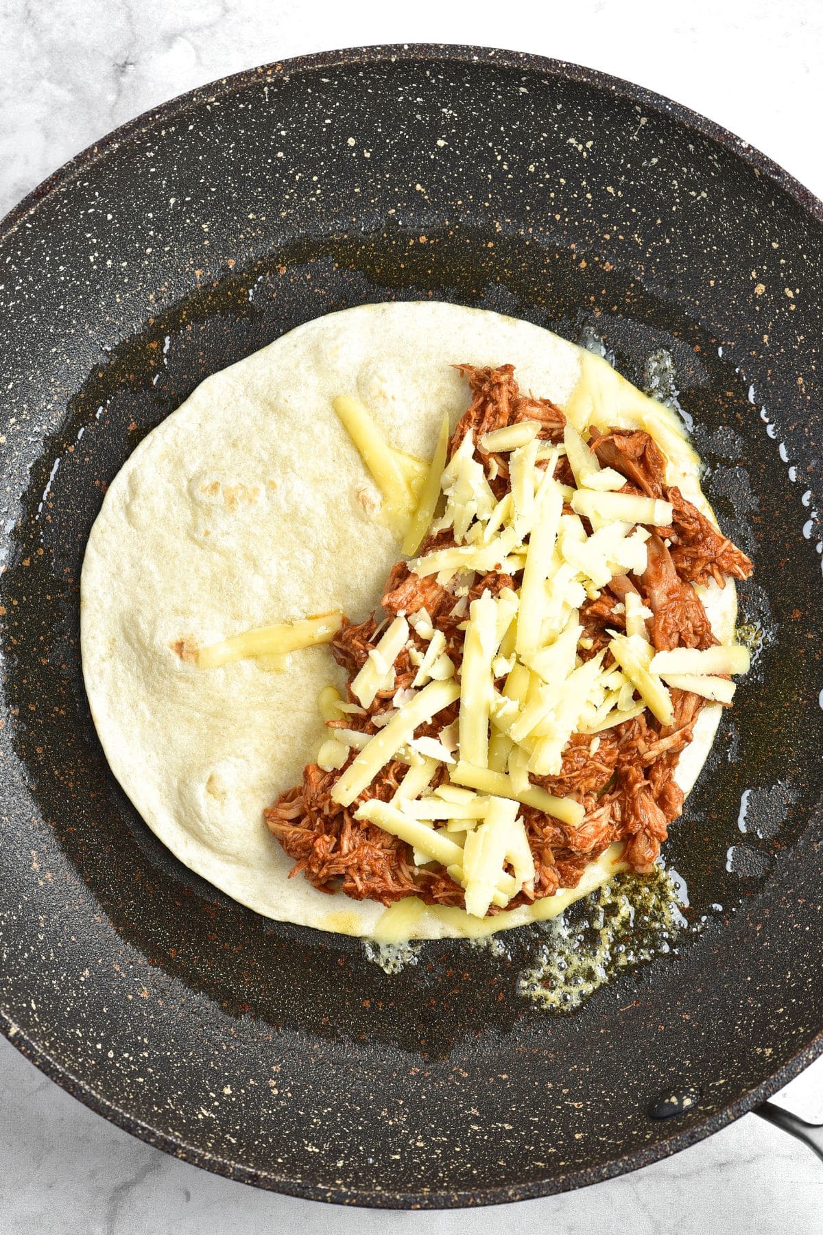 A skillet with a tortilla topped with shredded chicken and cheese.