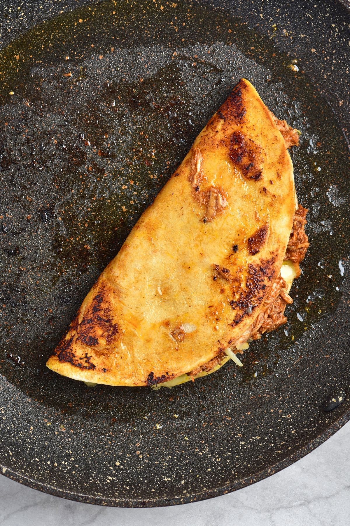 Cooking birria chicken taco in skillet