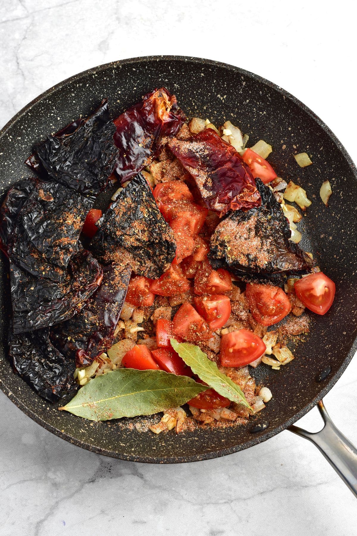 Sautéed onions, tomatoes, dried chiles, bay leaves in skillet.