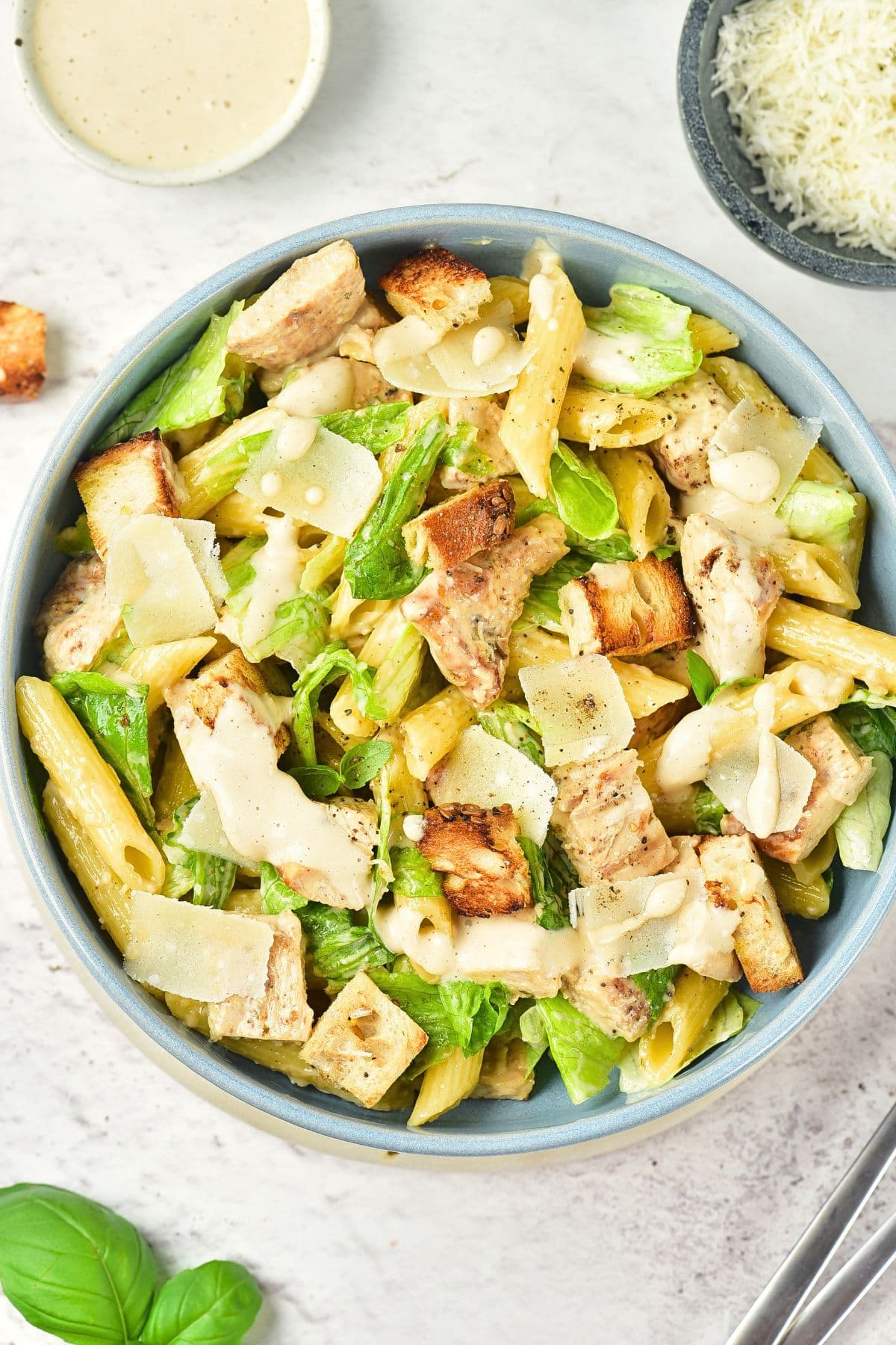 Top down view of a bowl of chicken caesar pasta salad on marble board.