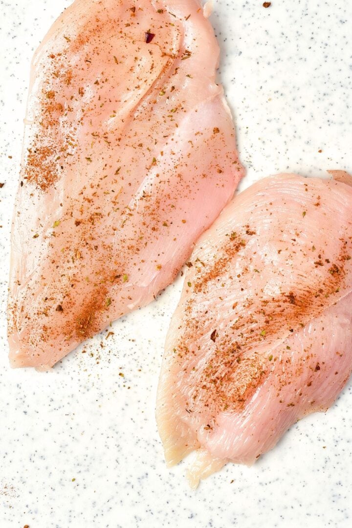 Seasoned chicken breast fillets on chopping board