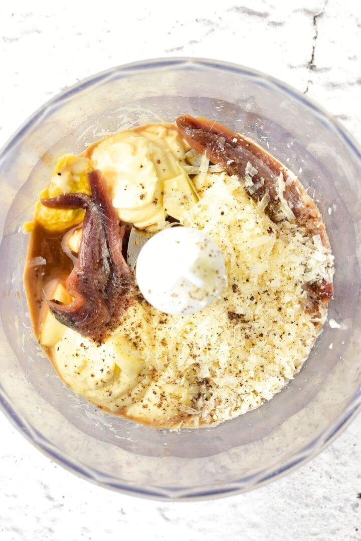 Grated dairy-free parmesan, mayonnaise, worcestershire sauce, anchovies, and Dijon mustard in a food processor bowl.